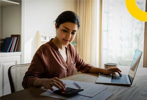 Una auxiliar contable validando datos con su calculadora y portátil.