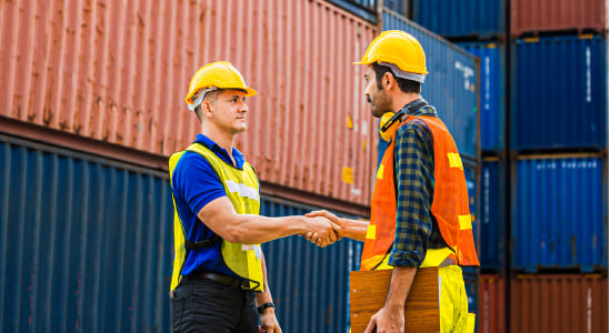 Dos hombres dándose la mano cerca de contenedores y centros de distribución.