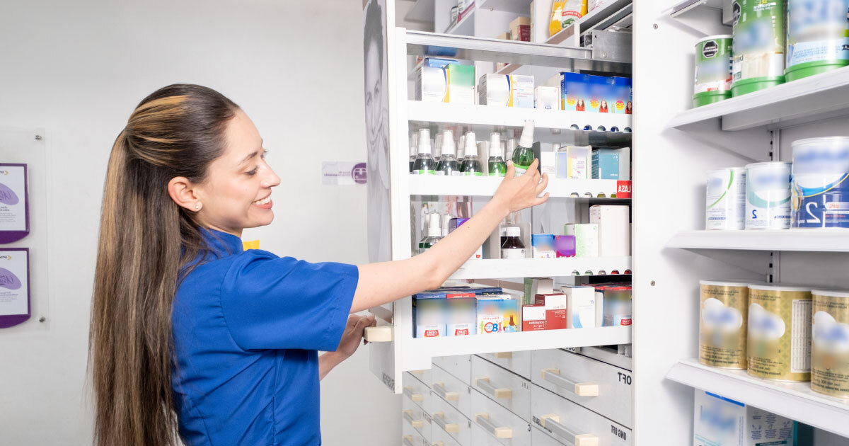 Profesional de la salud con uniforme azul sonríe frente a estantería de medicamentos