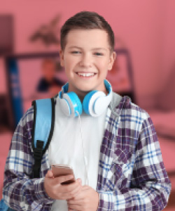 Hay un niño sonriendo con su celular en la mano y audífonos estudiando inglés en CET.